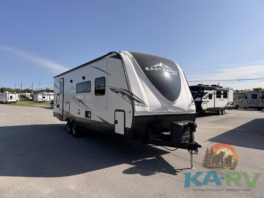 Travel trailer in outdoor lot with clear blue sky, branded East to West M-2600KRB.