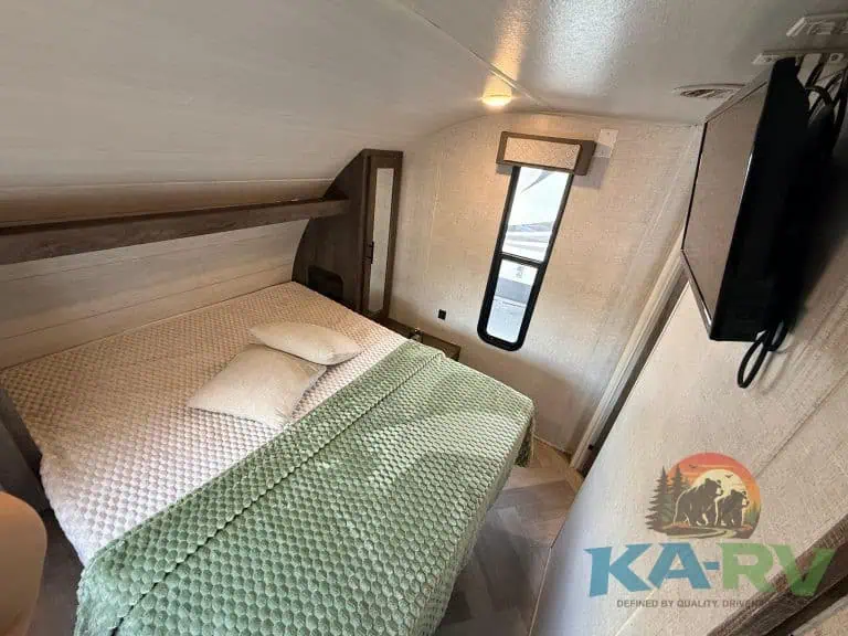 Interior of a cozy RV bedroom with a large bed and window view.
