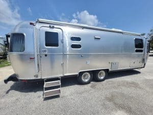 Classic silver Airstream travel trailer with entry steps and windows.