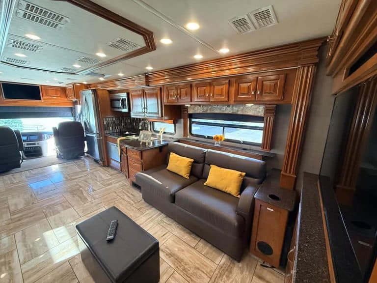 Interior of a luxury RV with wood cabinets, sofa, and kitchen area.
