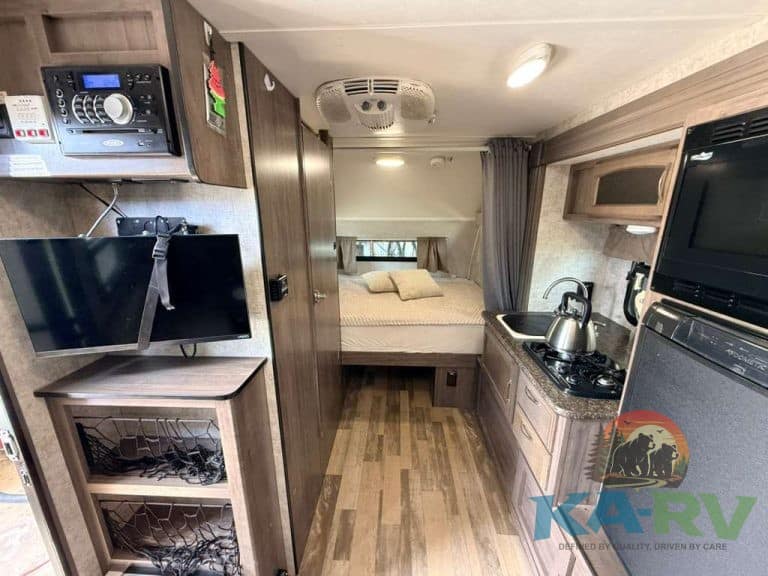 Cozy RV interior with bed, kitchen, and entertainment system.