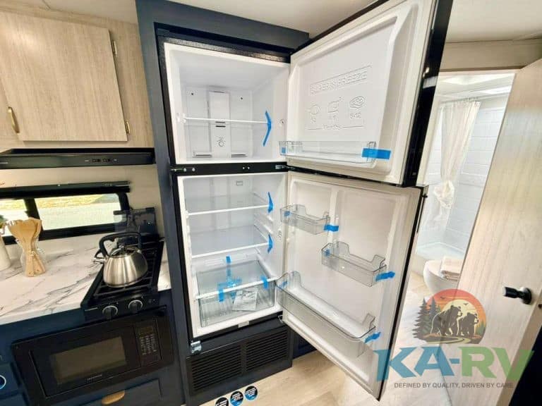 Open RV refrigerator showing empty interior with blue tape on shelves.