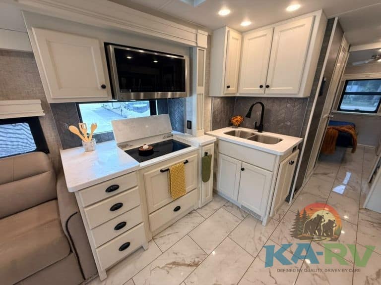 Modern RV kitchen with white cabinets and black appliances in Tiffin Allegro Bay 38AB.