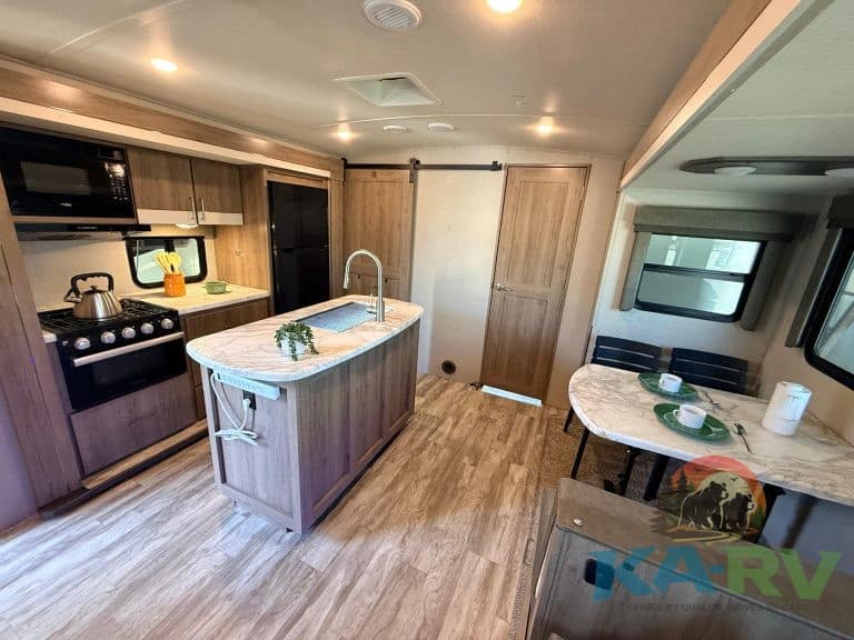 RV kitchen with modern appliances, cozy dining area, and wood finishes for optimal comfort and funct.
