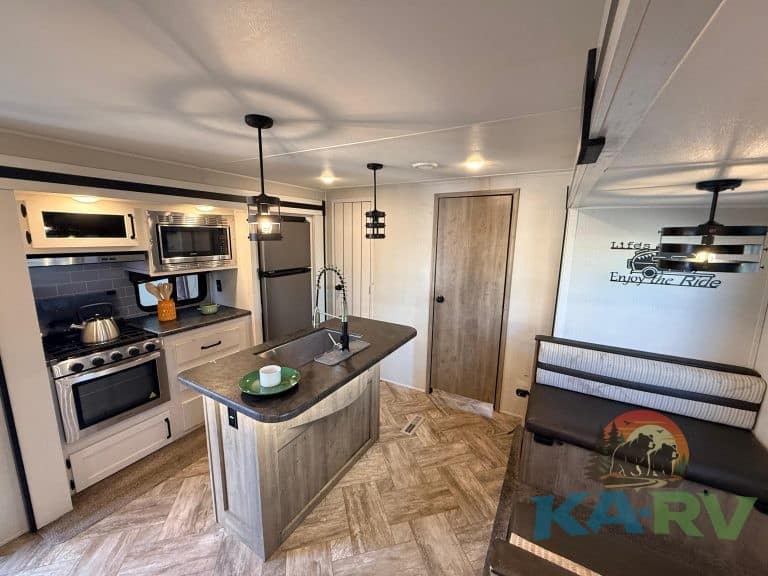 Modern RV kitchen with appliances, island, and dining space.