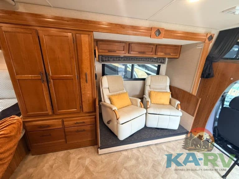 Cozy RV interior with two cream recliners and wooden cabinetry.