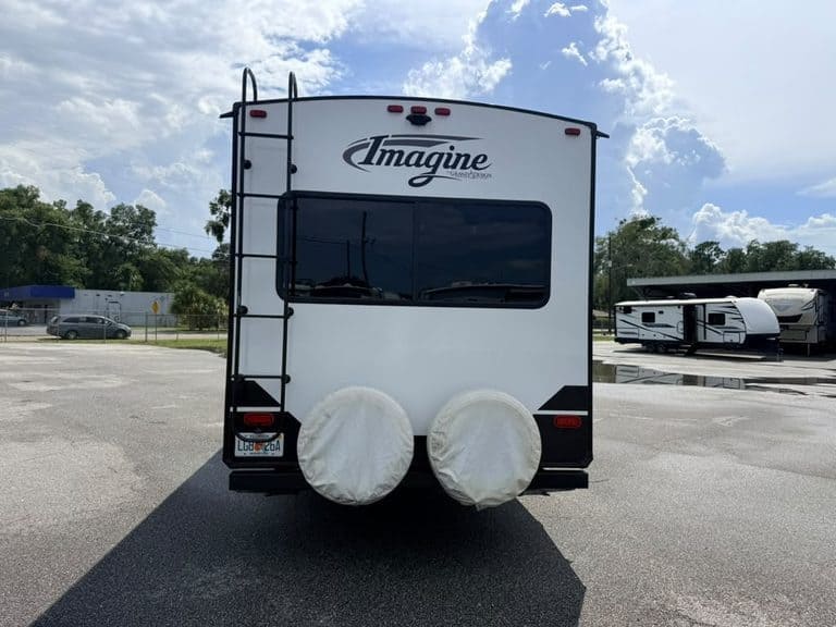 Rear view of white Imagine RV travel trailer with spare tires and ladder.