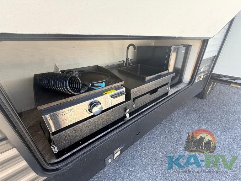 Outdoor kitchenette with sink and stove for Optima RVs, ideal for camping and travel comfort.