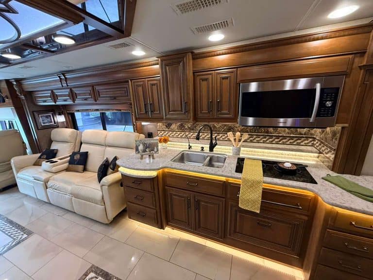 Modern RV kitchen with wooden cabinets, microwave, and sofa.