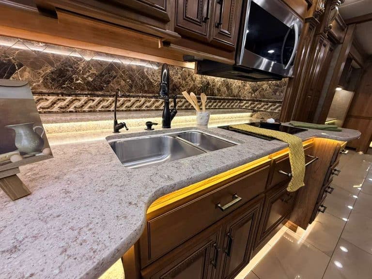 Modern RV kitchen with granite countertops and dark wood cabinets.