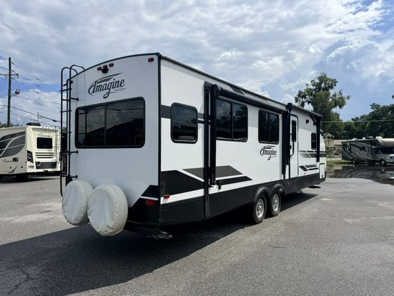 White Imagine RV travel trailer with black accents parked outdoors.