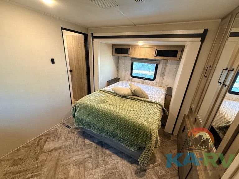 RV bedroom interior with storage cabinets, window, and cozy bed for optimal comfort.