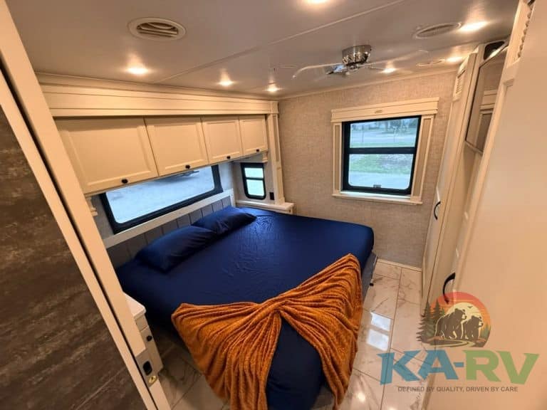 RV bedroom interior with large window, bed, and storage cabinets.