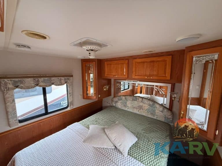 RV bedroom with wooden cabinets, large window, and cozy bed setup for optimal comfort.