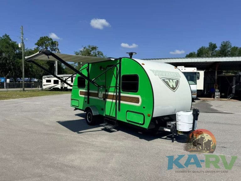 Compact green and white travel trailer with awning at RV dealership.