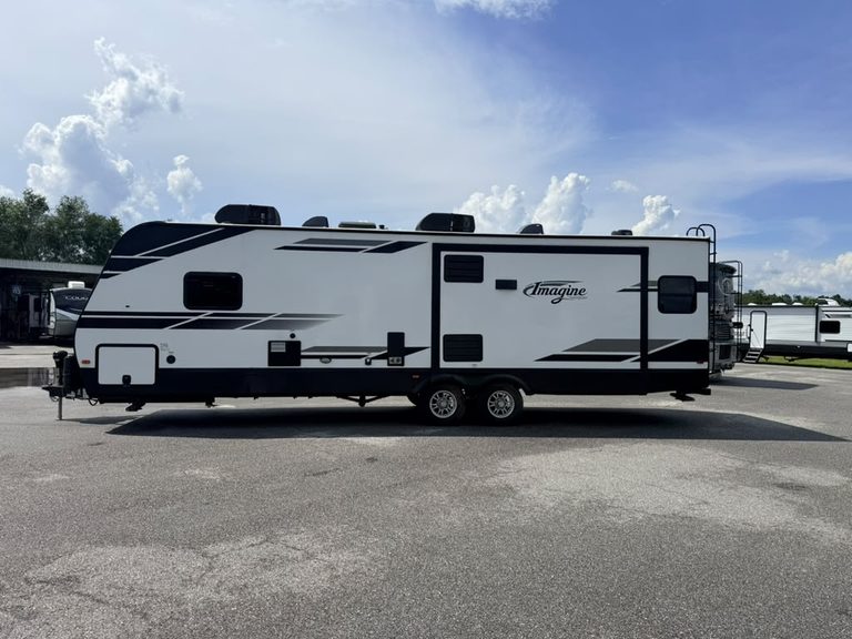 Modern white RV travel trailer with black accents at Karv Repair lot.