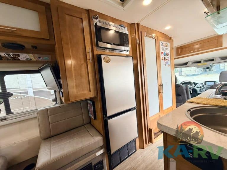 RV kitchen with refrigerator, microwave, and seating area.