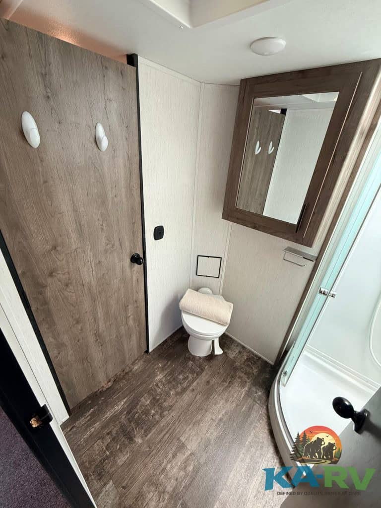 Bathroom interior with toilet, mirror, and shower in a Forest River Cherokee Wolf Pack RV.