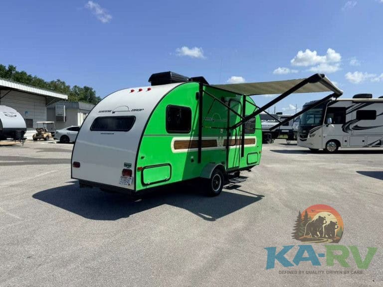 Green and white travel trailer with awning in parking lot.