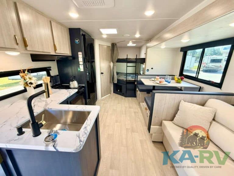 Modern RV interior with kitchen, sofa, and bunk beds for family travel.