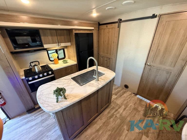 Modern RV kitchen with appliances, sink, and wooden cabinets for optimal space.