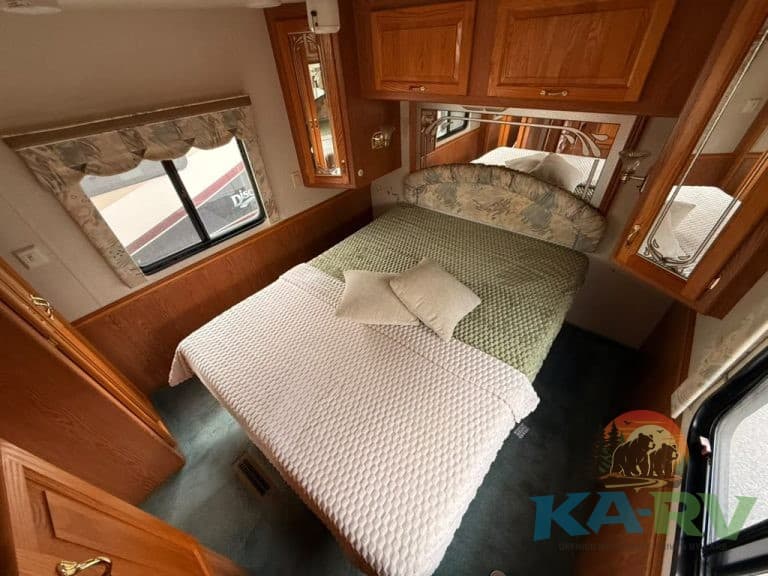 RV bedroom interior with wooden cabinets, window view, and cozy bedding for optimal comfort.