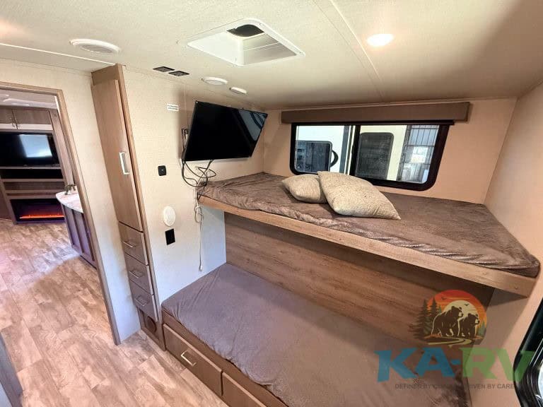 Efficient RV bedroom with bunk beds, wall-mounted TV, and cozy bedding for comfortable travel rest.