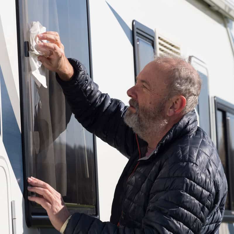Man cleaning RV window to prevent fogging and improve visibility.