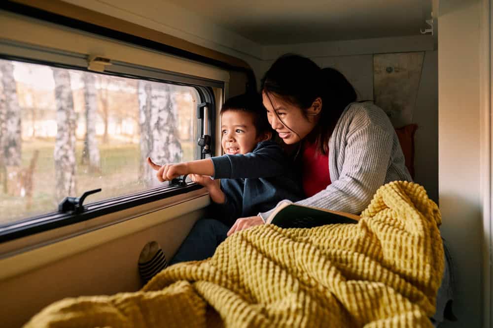 Little boy points out RV window with his mom, wrapped in a blanket.