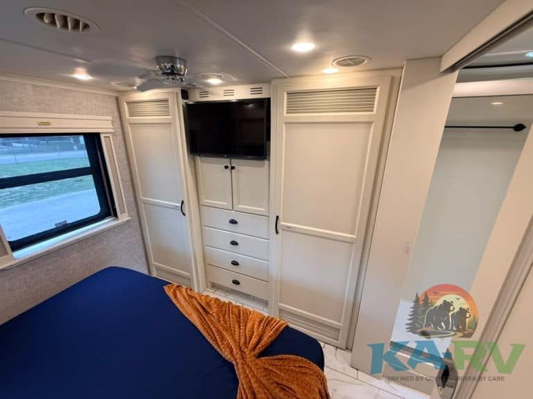 RV bedroom interior with TV, storage, and window view.
