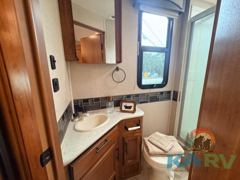 Interior view of a clean RV bathroom with wooden cabinets and a shower stall.