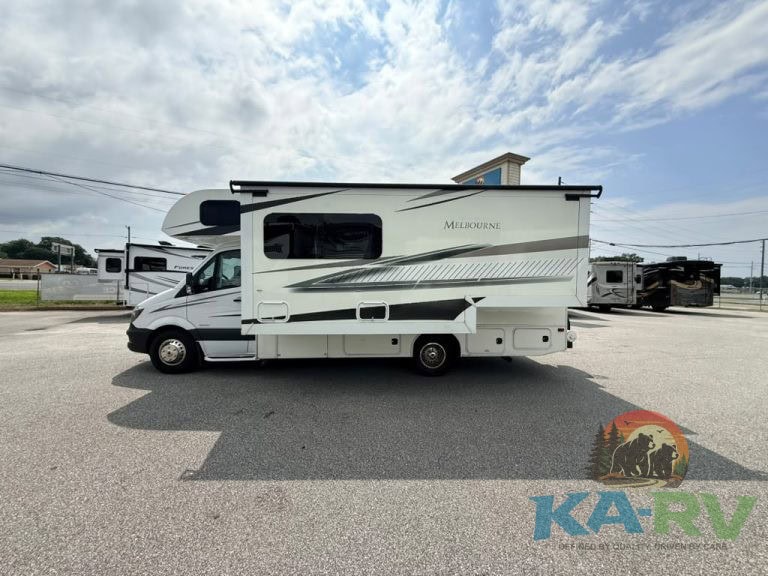 White travel trailer RV parked on asphalt with blue sky and clouds.