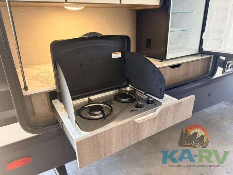 Outdoor RV kitchen with two-burner stove and weather-resistant cover for cooking convenience.