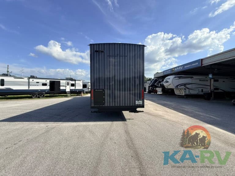 Black RV storage trailer in outdoor lot with RVs and blue sky.