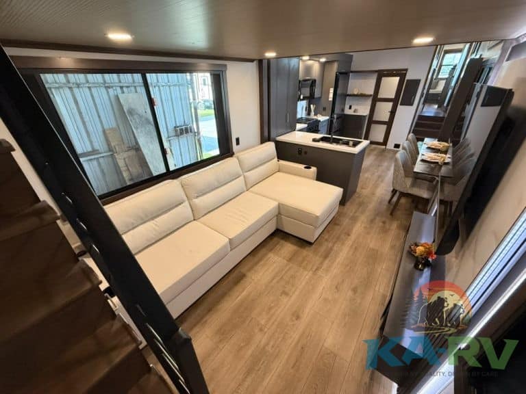 Spacious RV living room with white sectional sofa and kitchen area.