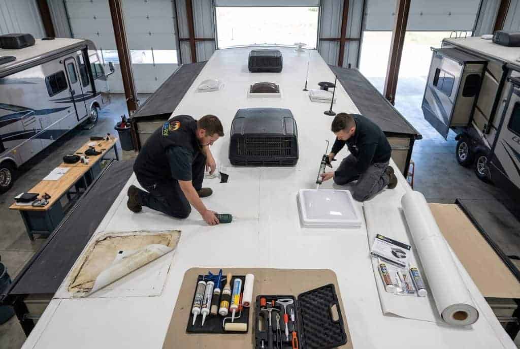 RV roof repair specialists working on a large RV roof in a service bay.