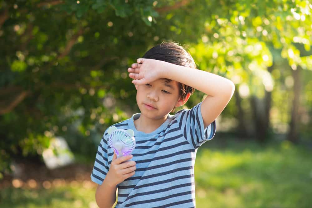 Child checking temperature with a handheld fan outdoors.