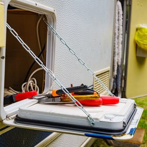 Open RV storage compartment with tools for summer prep and maintenance.