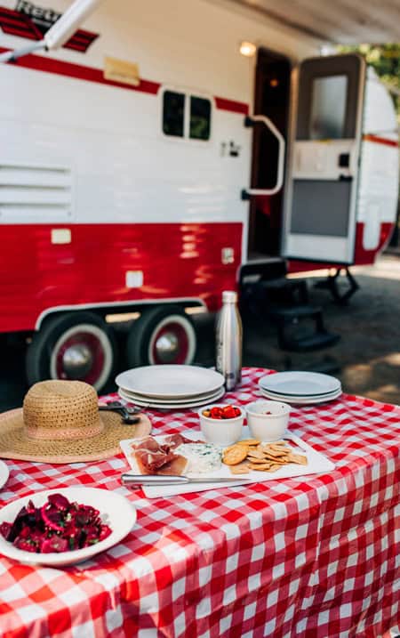Food spread out on a picnic table in front of an RV. A great Summer RV checklist starts with making sure you pack for summer activities