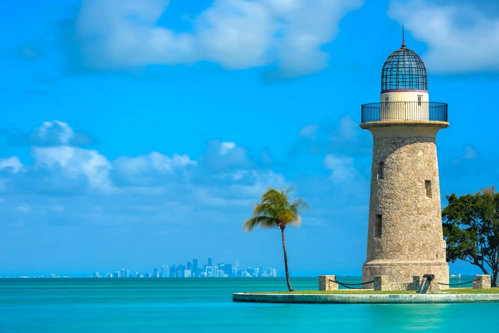 Lighthouse near the water with a palm tree, part of Florida's scenic coastal landscape.