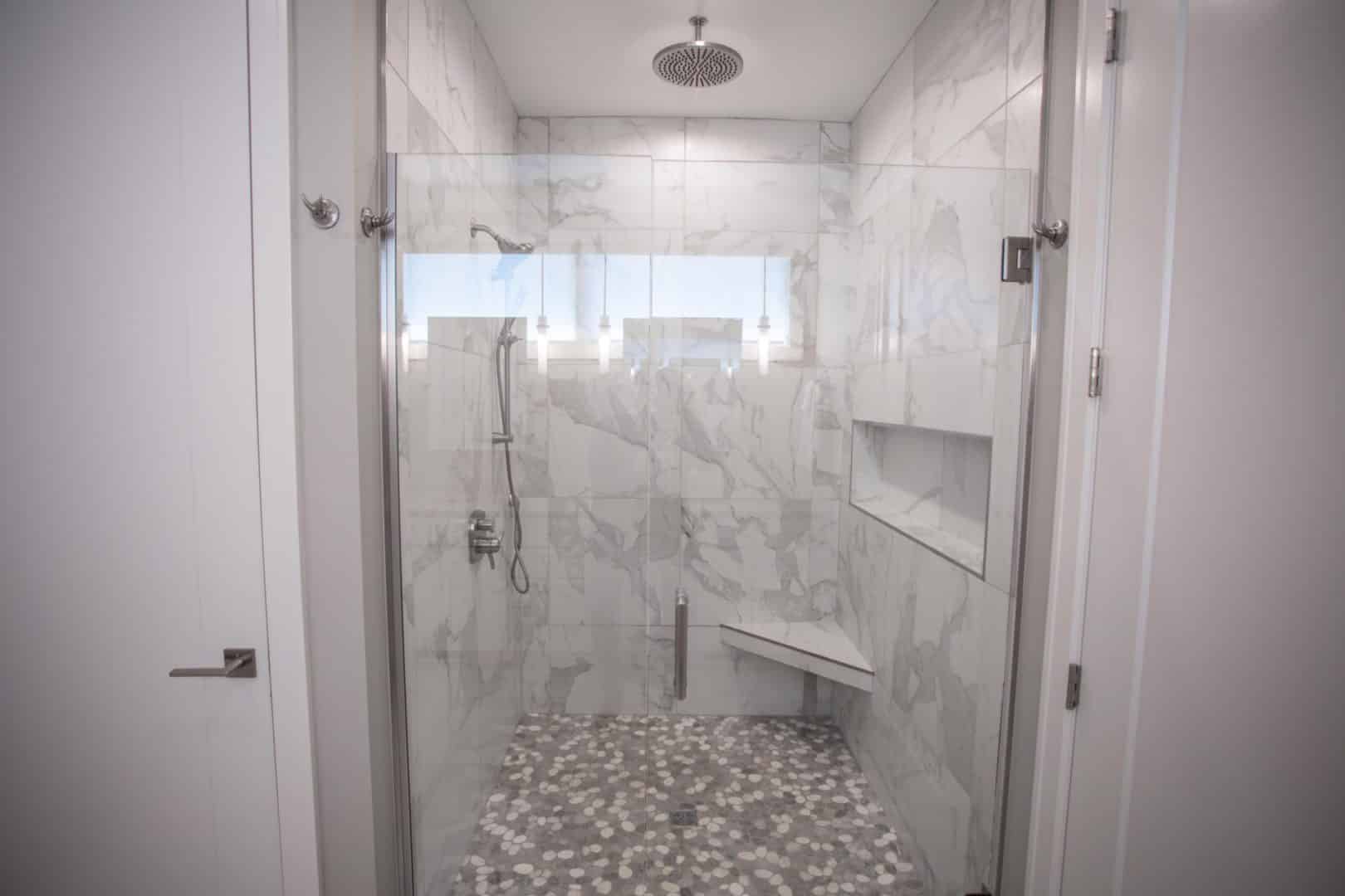 Modern marble shower with built-in bench and stylish pebble floor tiles.