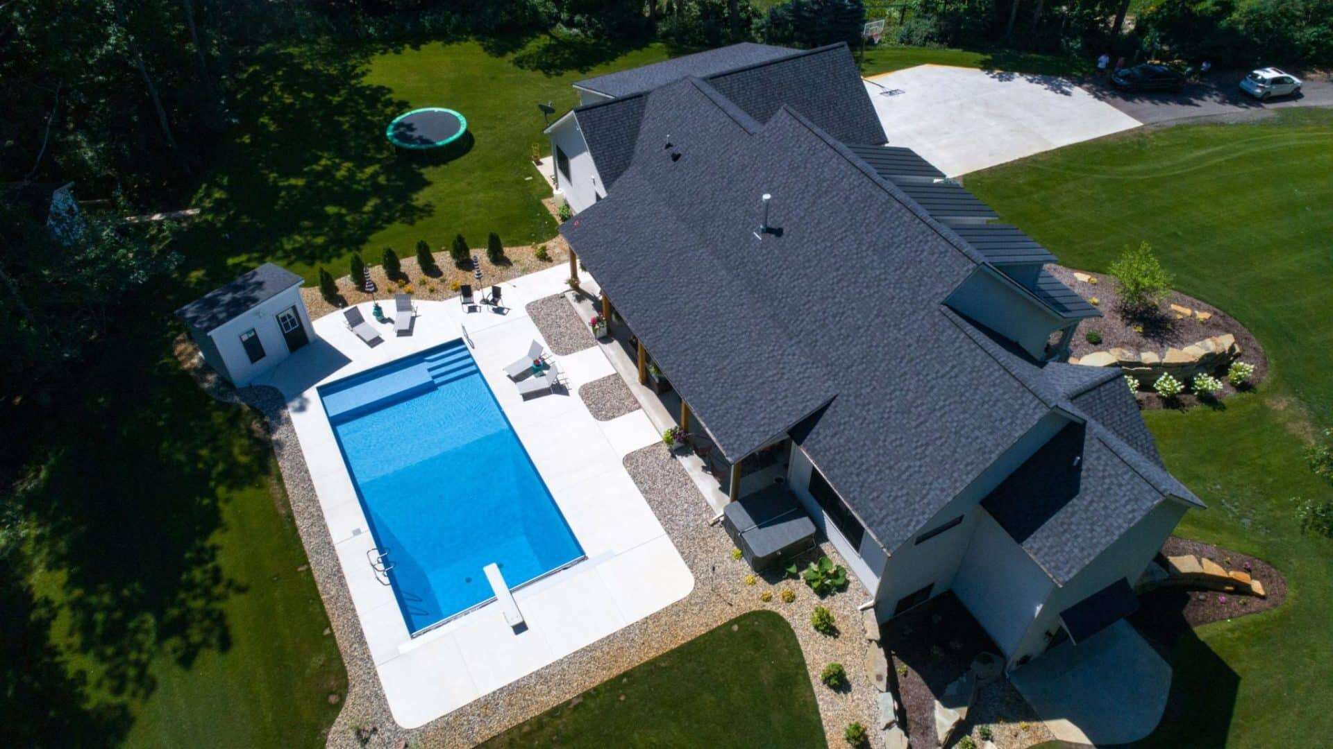 Aerial view of a modern house featuring a large swimming pool, lush green lawn, and outdoor seating.