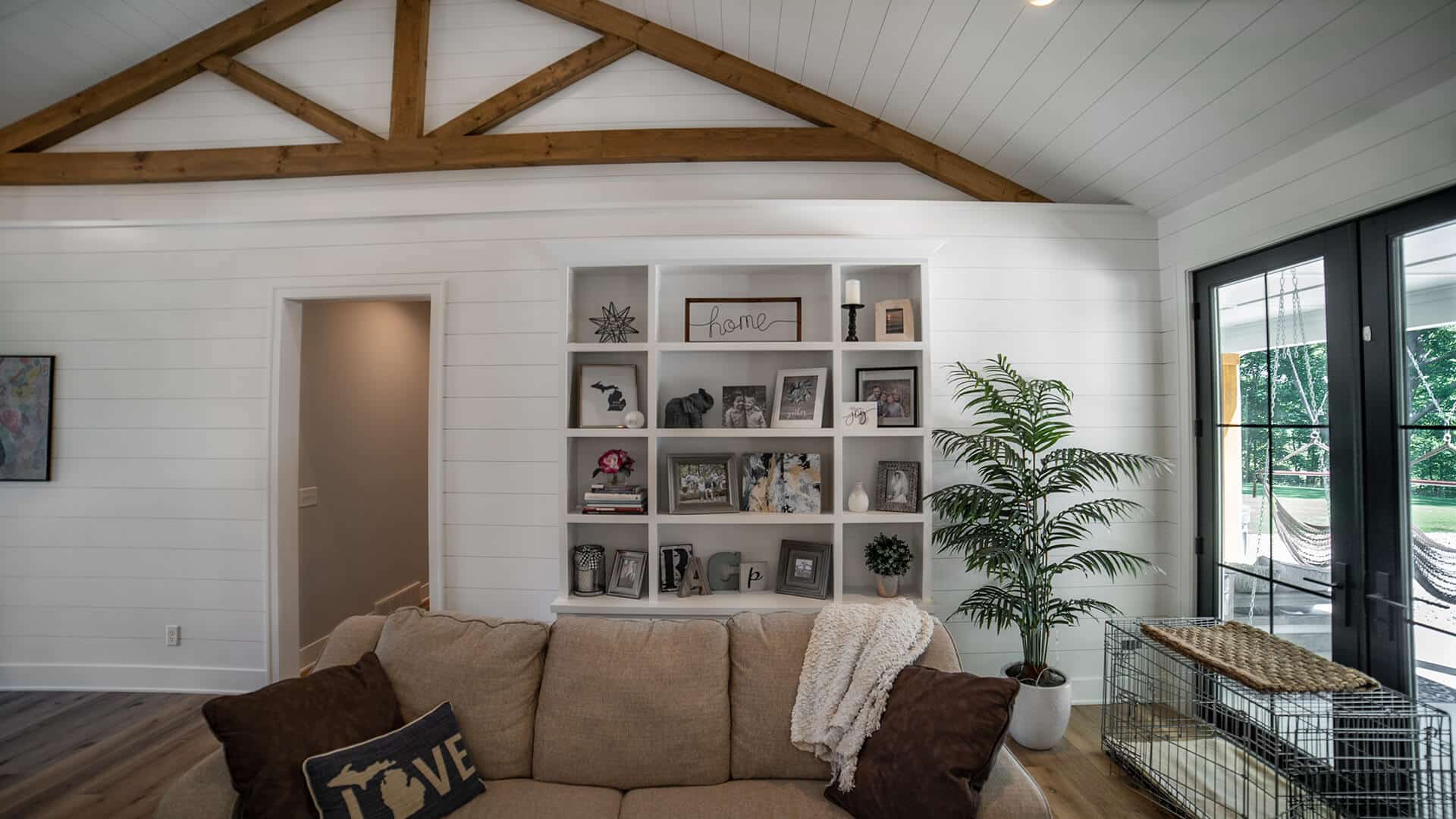 Modern living room with white walls, wooden beams, and large windows.