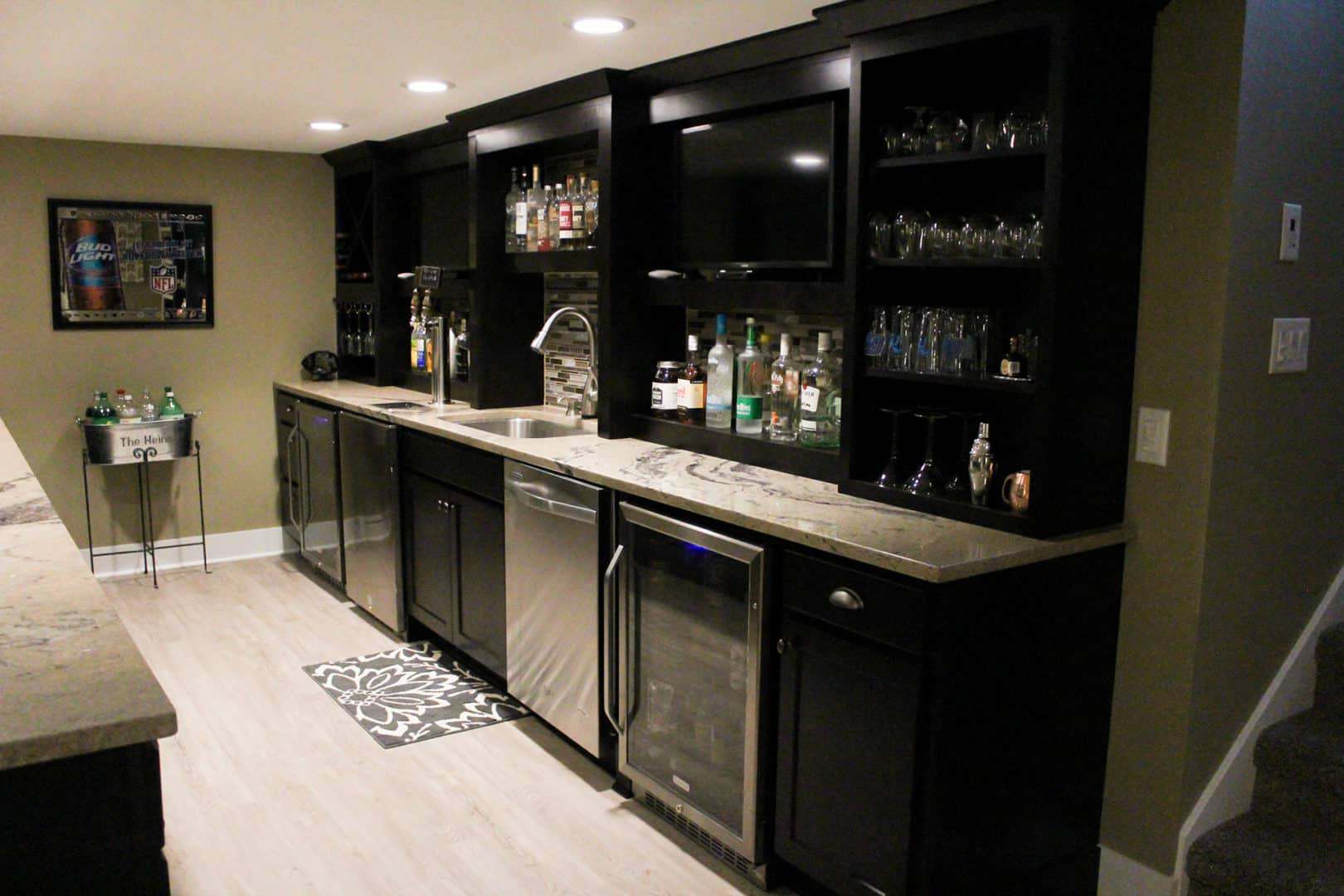 Modern home bar with black cabinetry, wine cooler, and glassware display.
