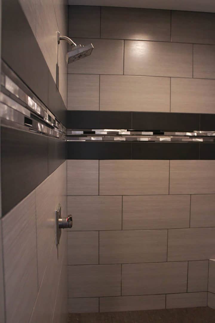 Contemporary bathroom shower featuring large gray tiles and decorative mosaic strip.
