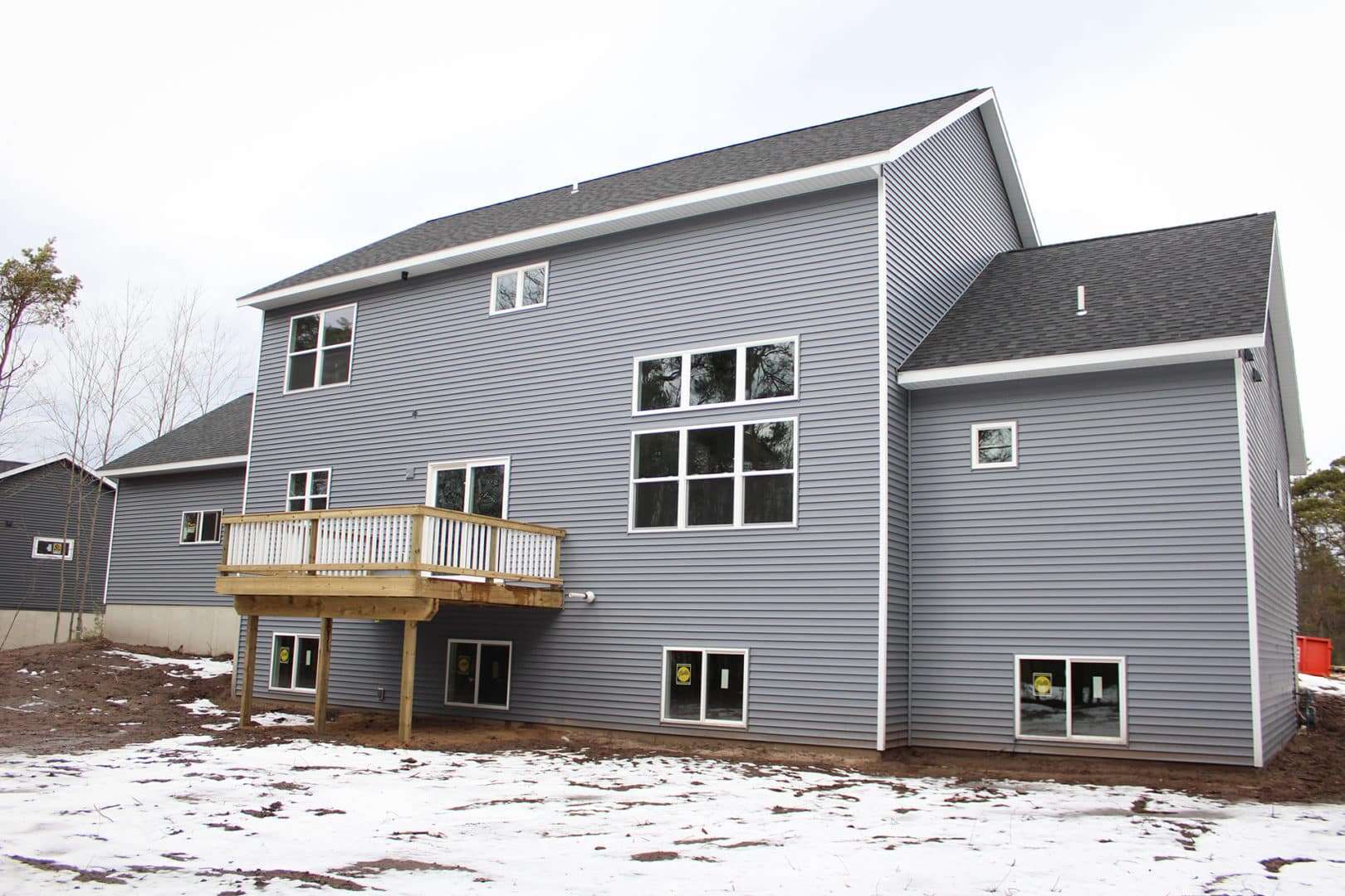 Blue siding house with large windows and a wooden deck, showcasing contemporary residential design.