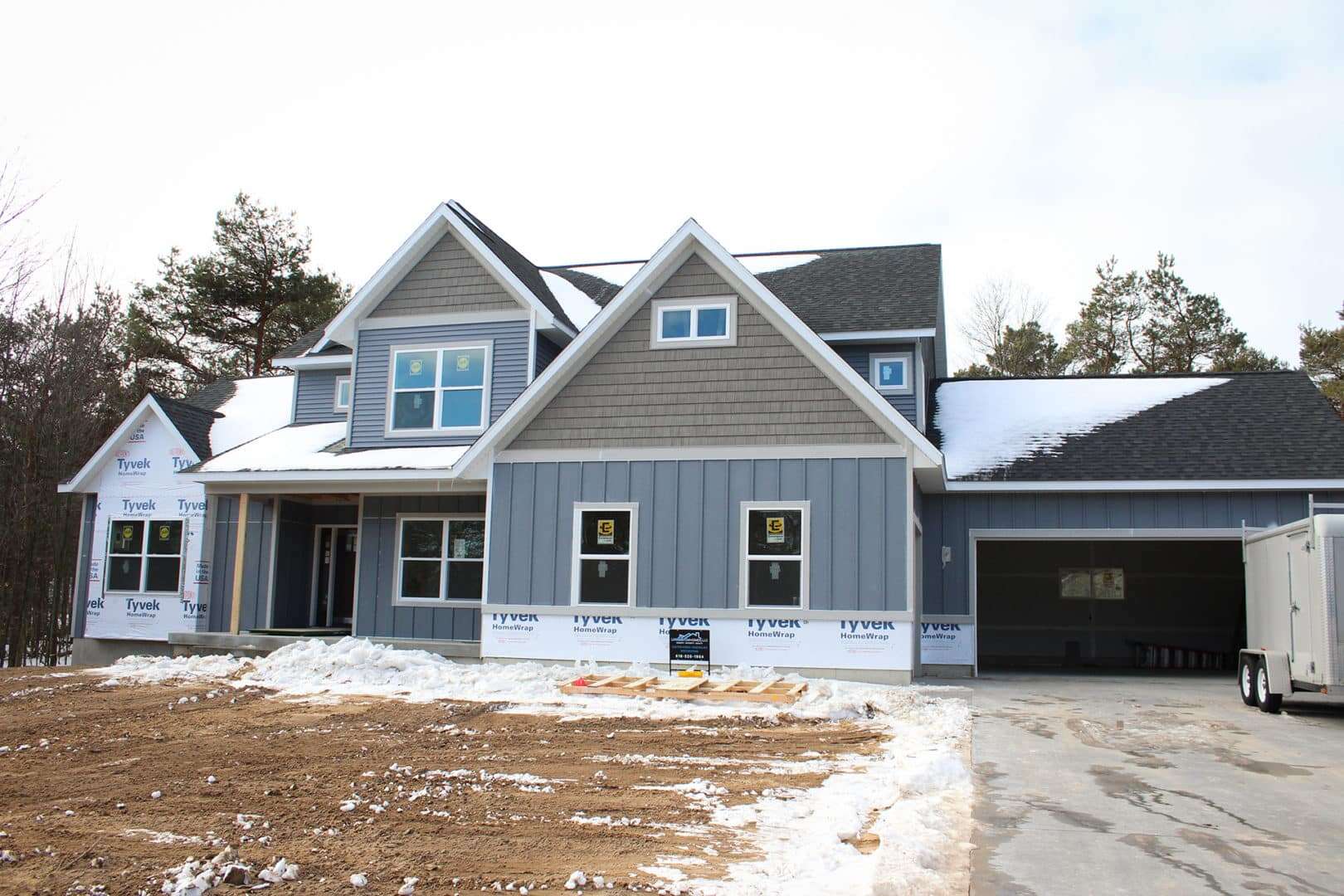 Modern new home under construction with blue siding and snow-covered yard.