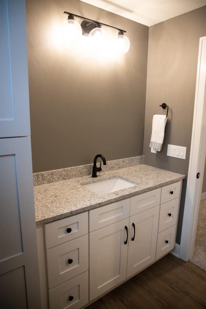 Bathroom vanity with granite top, black faucet, and wall-mounted light fixture.