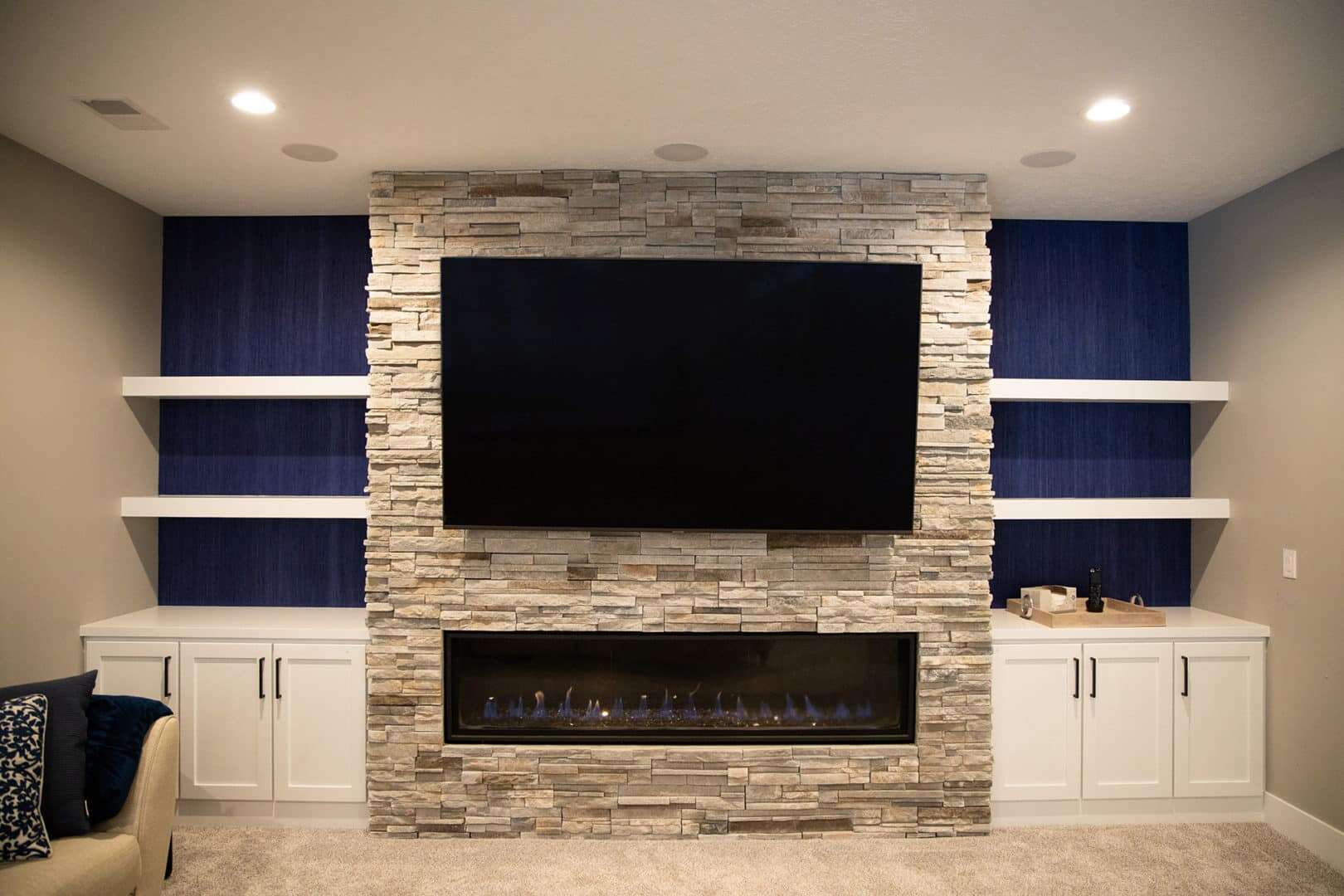 Living room with stone fireplace, flat-screen TV, and built-in white shelves for a stylish, cozy spa.