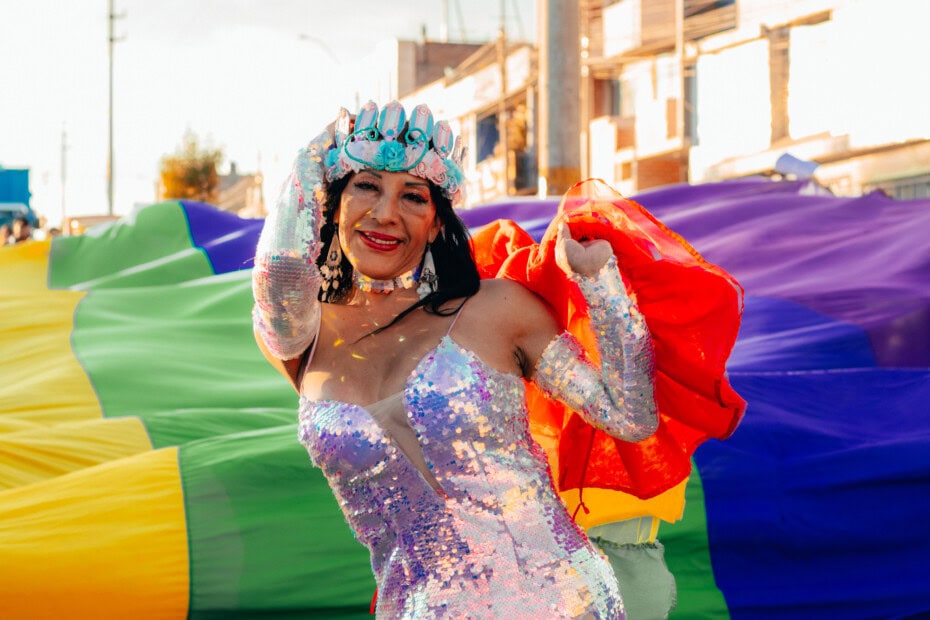 trans woman in sequin dress looking happy with Pride flag
